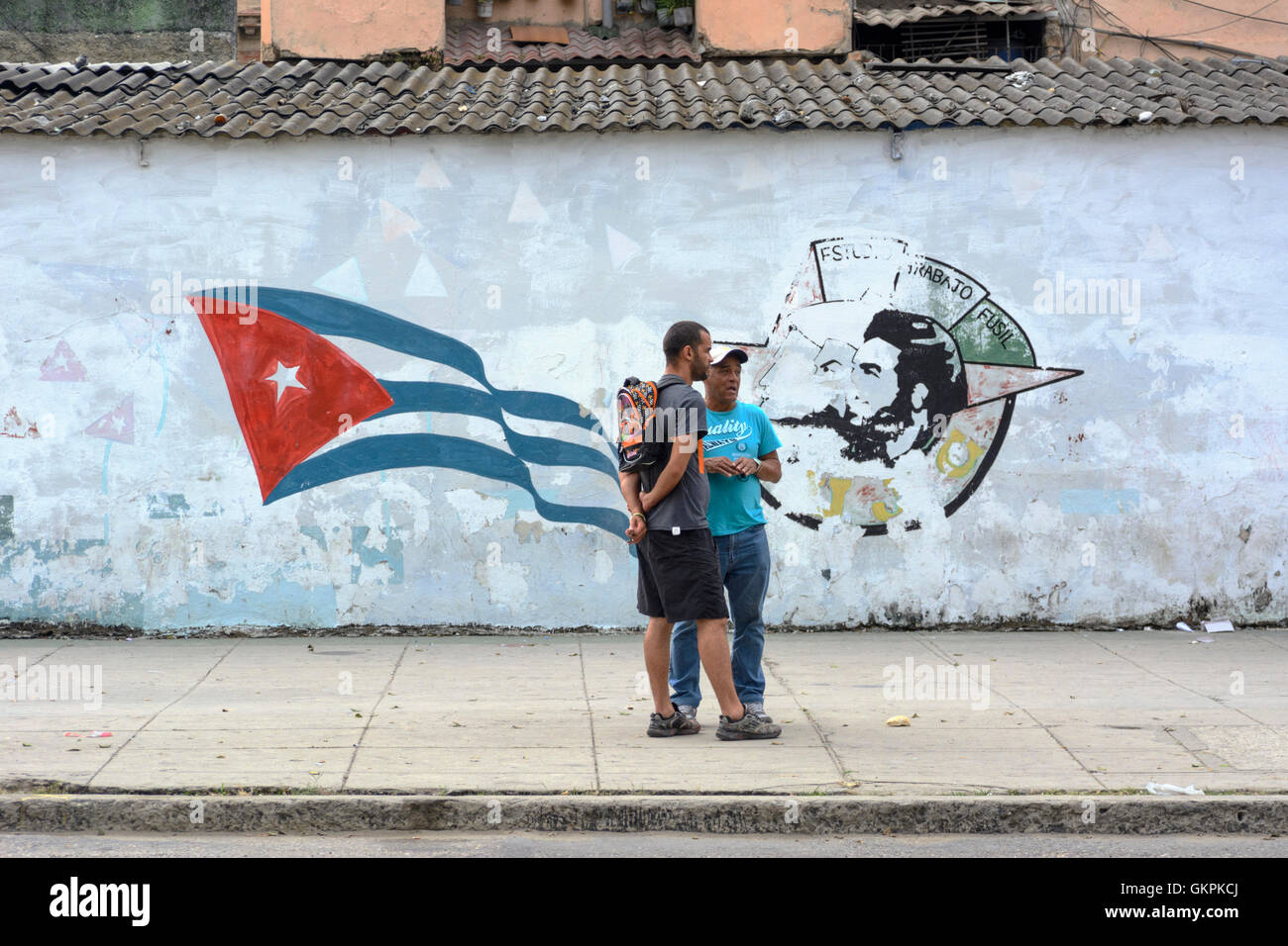 Due uomini cubani in piedi di fronte a un rivoluzionario murale su una parete a l'Avana Vecchia (La Habana Vieja), Cuba Foto Stock