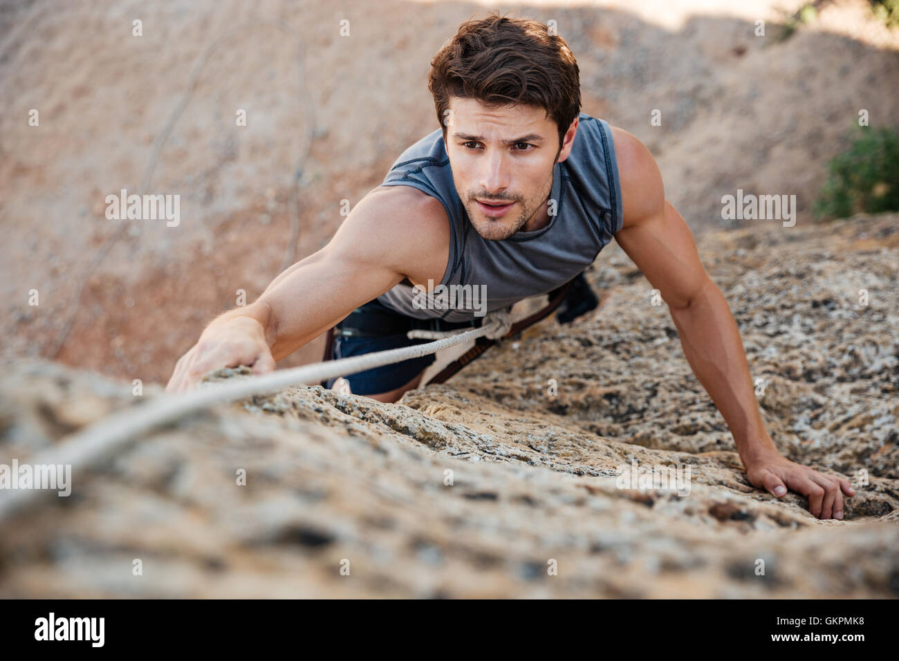 Uomo di raggiungere per un grip mentre lui rock si arrampica su di una ripida scogliera Foto Stock