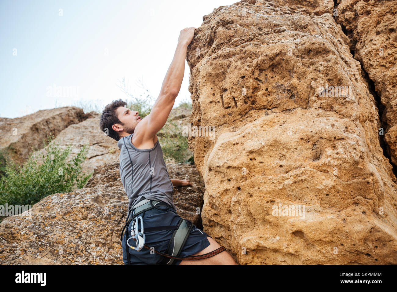 Uomo di raggiungere per un grip mentre lui rock si arrampica su di una ripida scogliera Foto Stock