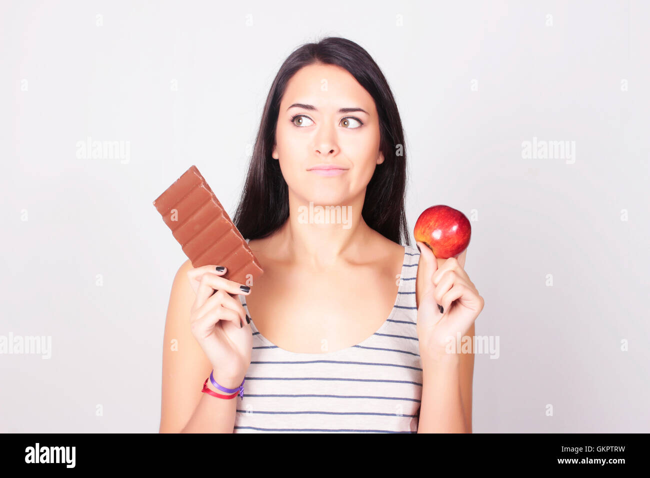 Giovane donna caucasica di effettuare una scelta tra cioccolato e Apple. Fitness e il concetto di dieta. Foto Stock