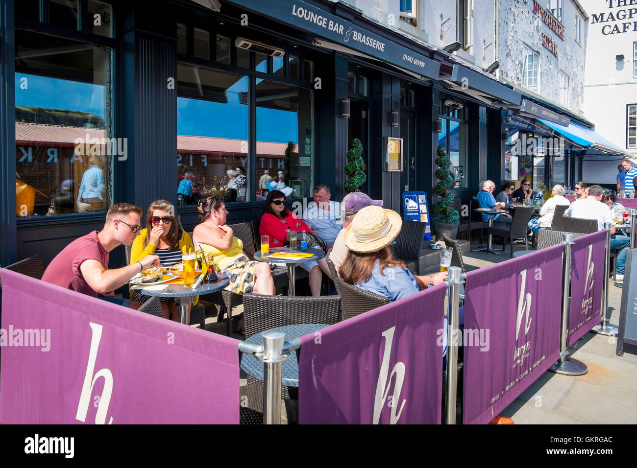 Le persone che si godono il ristoro seduto fuori Harrys Lounge Bar Brasserie in Pier Road Whitby estate Foto Stock