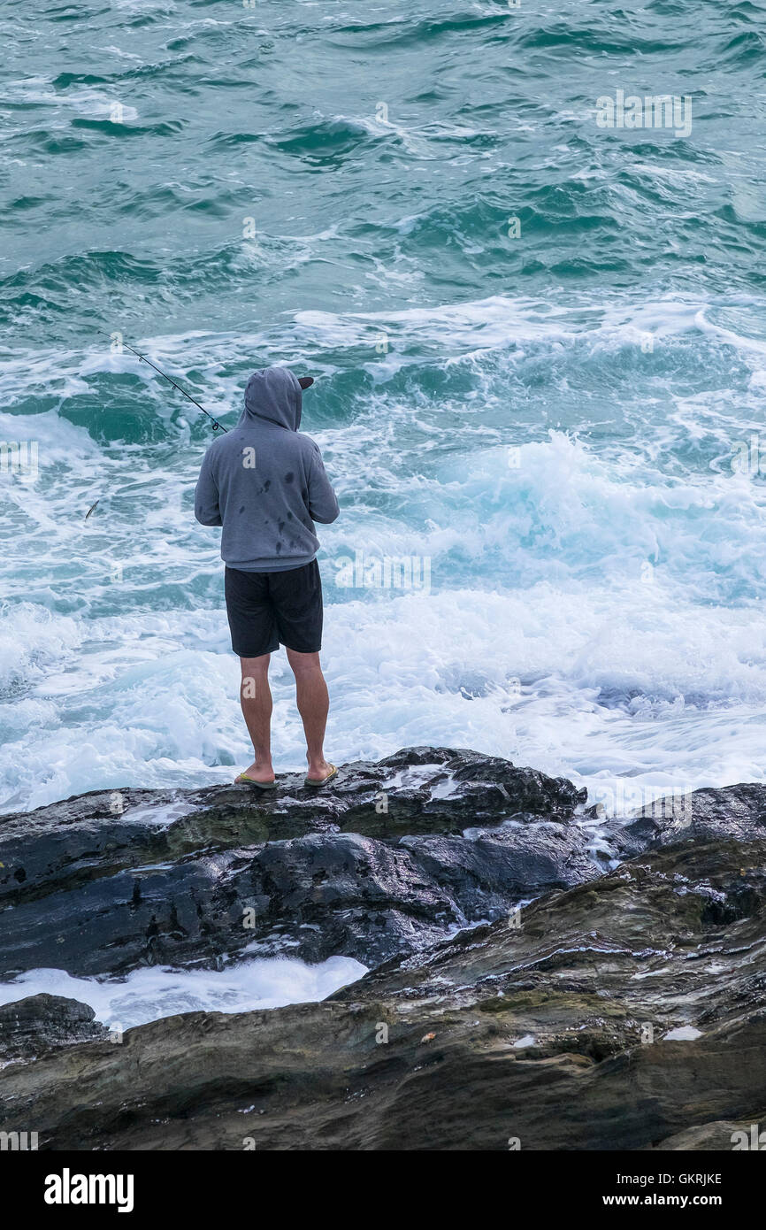 Un vacanziere pesca dalle rocce a Newquay, Cornwall. Foto Stock