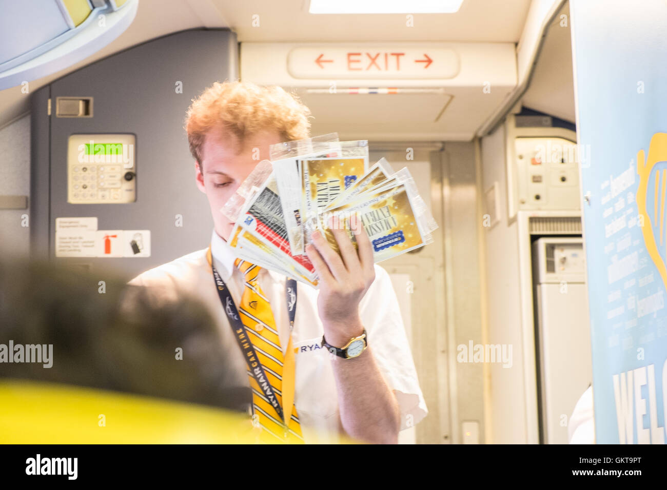 Assistente di Volo steward cercando di vendere le schede della graffiatura a bordo in cabina di volo Ryanair. Foto Stock
