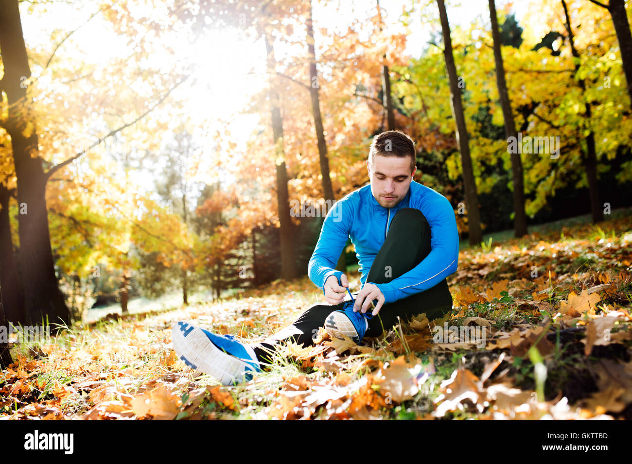 Runner seduto a terra, la legatura lacci delle scarpe, la natura in autunno Foto Stock