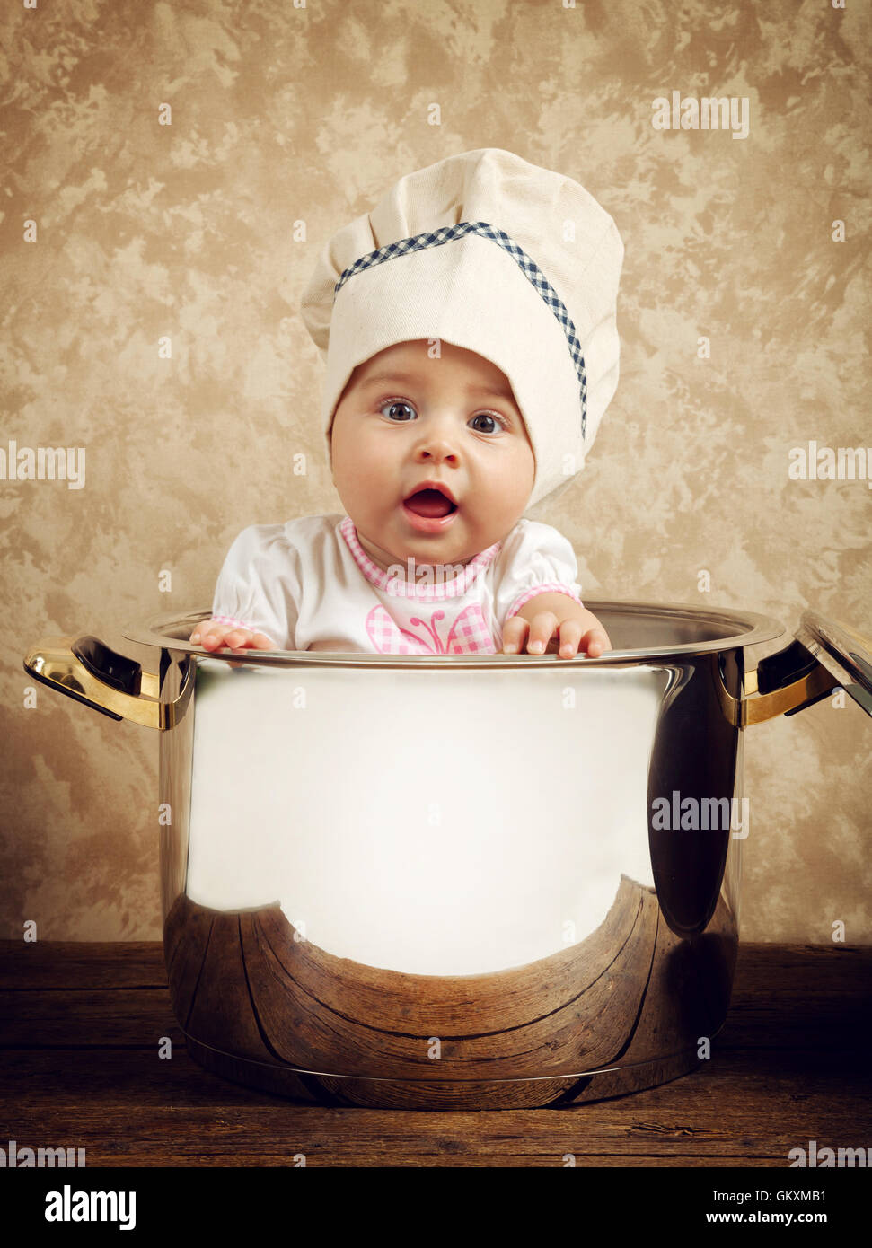 Carino baby chef in un immenso calderone sul tavolo di legno Foto Stock