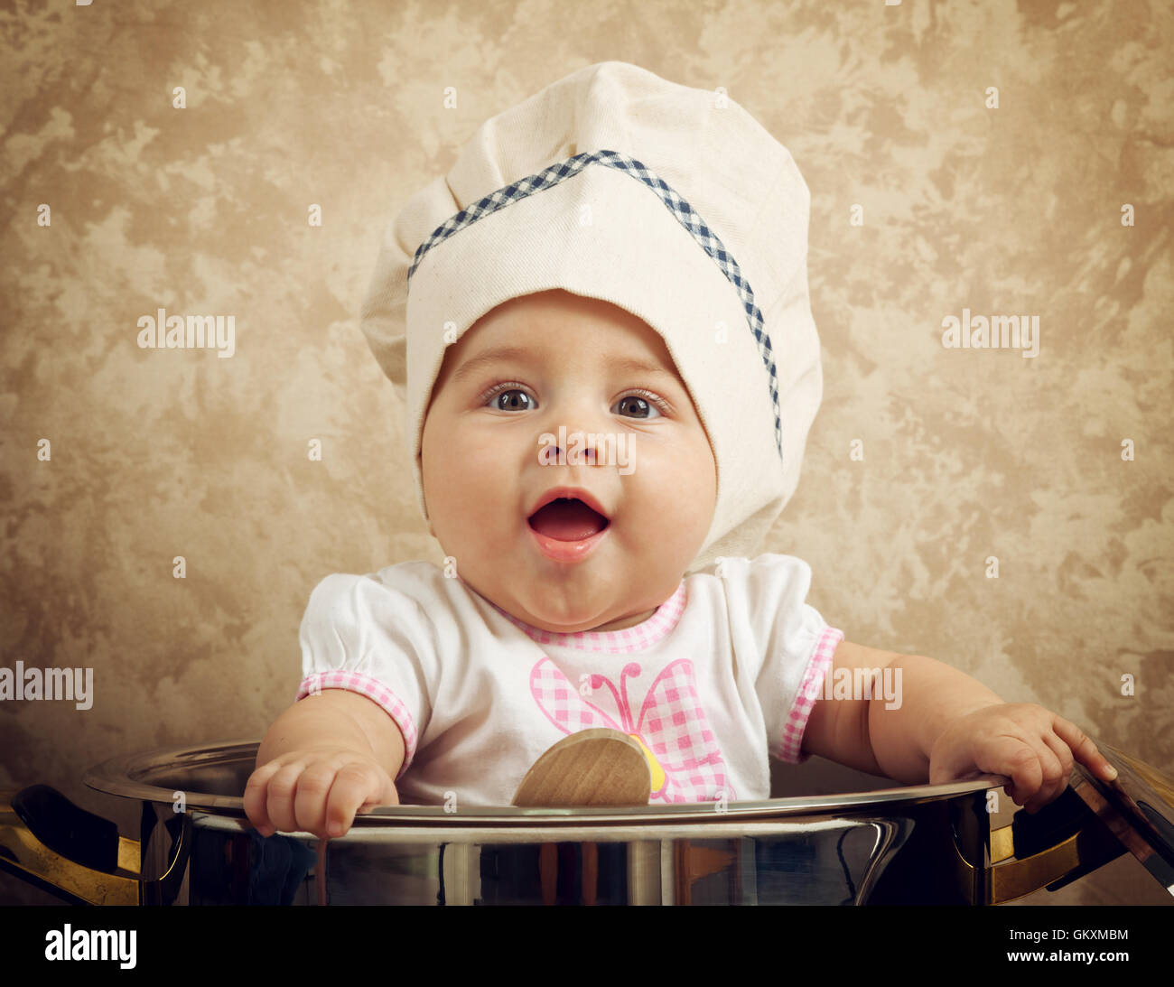 Carino baby chef in un immenso calderone sul tavolo di legno Foto Stock