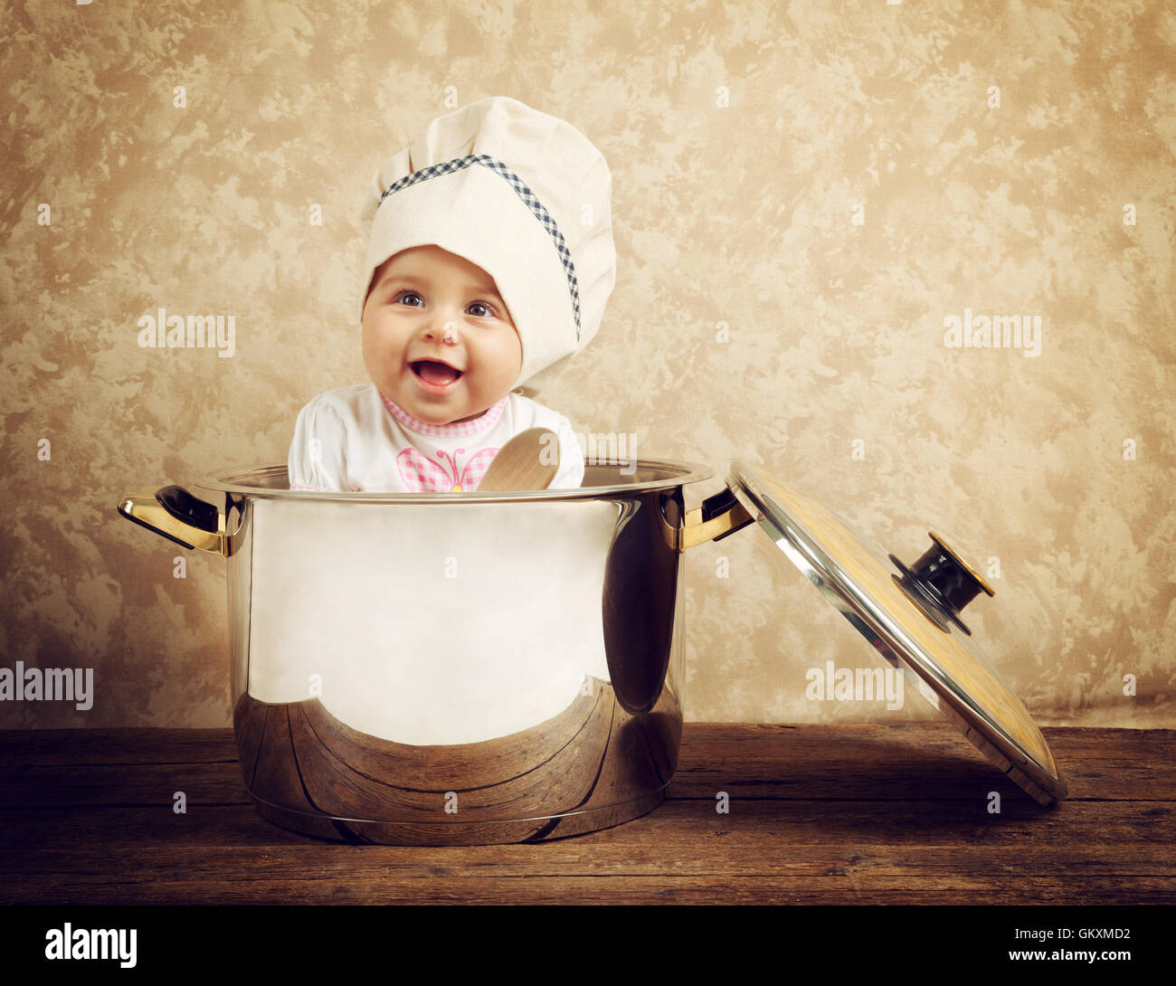 Carino baby chef in un immenso calderone sul tavolo di legno Foto Stock