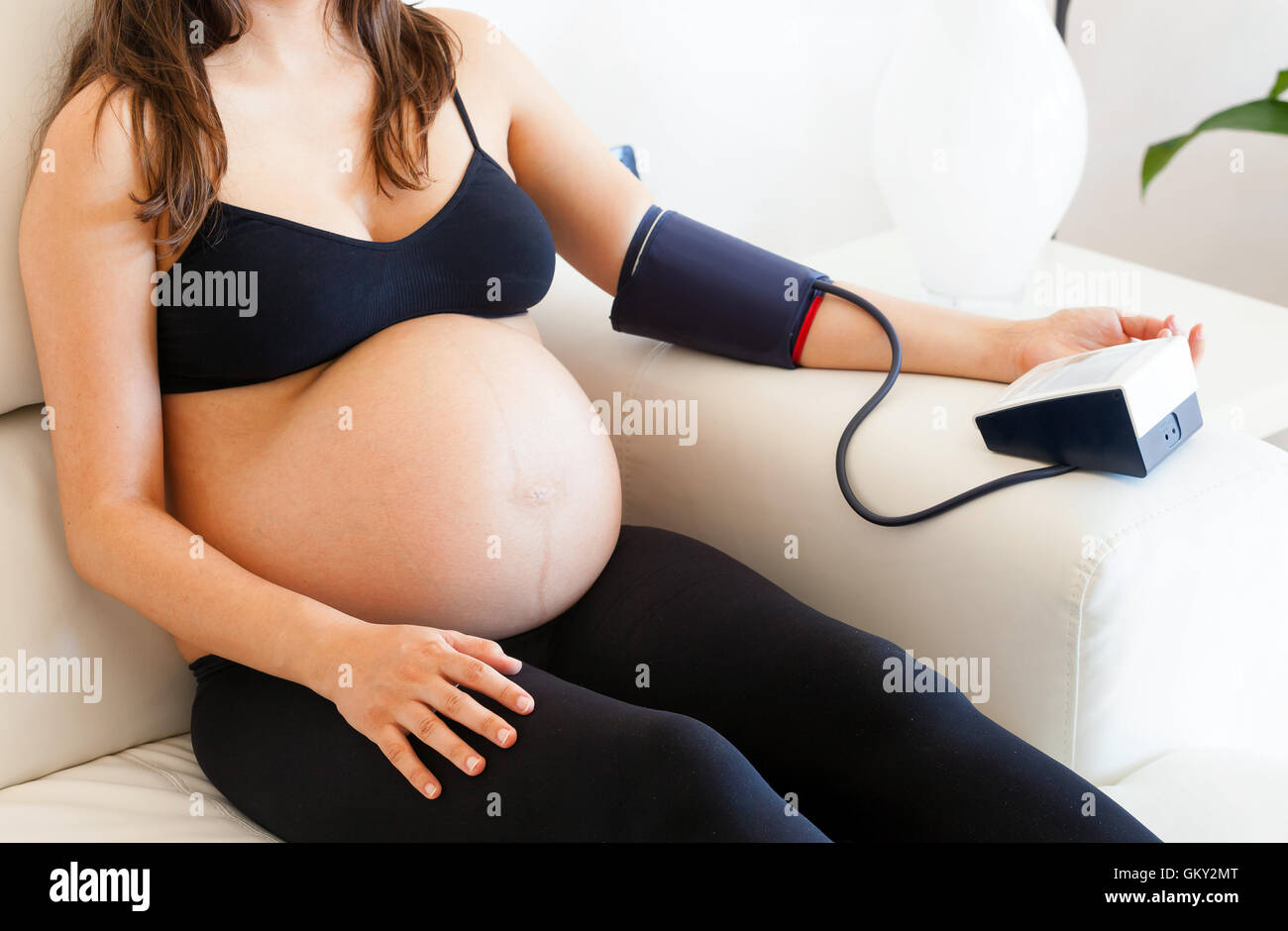 Donna incinta misura la pressione sanguigna con sfigmomanometro automatico. Foto Stock