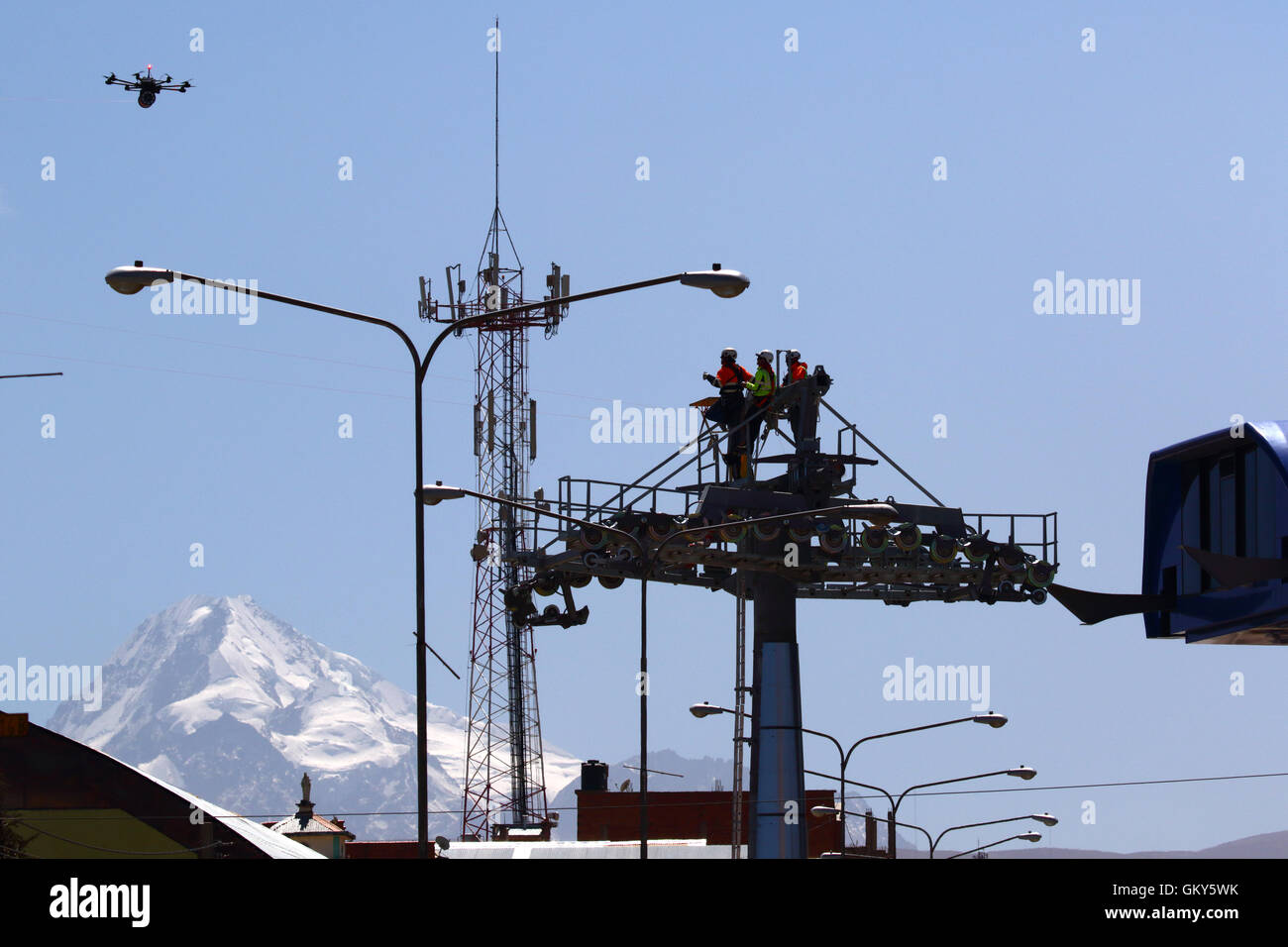 El Alto, Bolivia, 23 agosto 2016.I tecnici di attendere per un drone che sta portando una luce cavo sintetico tra i piloni di una nuova cabinovia / telecabina che è in costruzione. Questa è la prima parte del processo di installazione finale del cavo in acciaio che portano le gondole. Questo cavo auto tra Rio Seco e la Ceja a El Alto è uno di una seconda fase di linee della cabinovia che fanno parte di un progetto ambizioso per alleviare la congestione del traffico. 3 tratte dalla prima fase sono già operativi tra le città di La Paz e El Alto. Mt Huayna Potosi è in background. Foto Stock