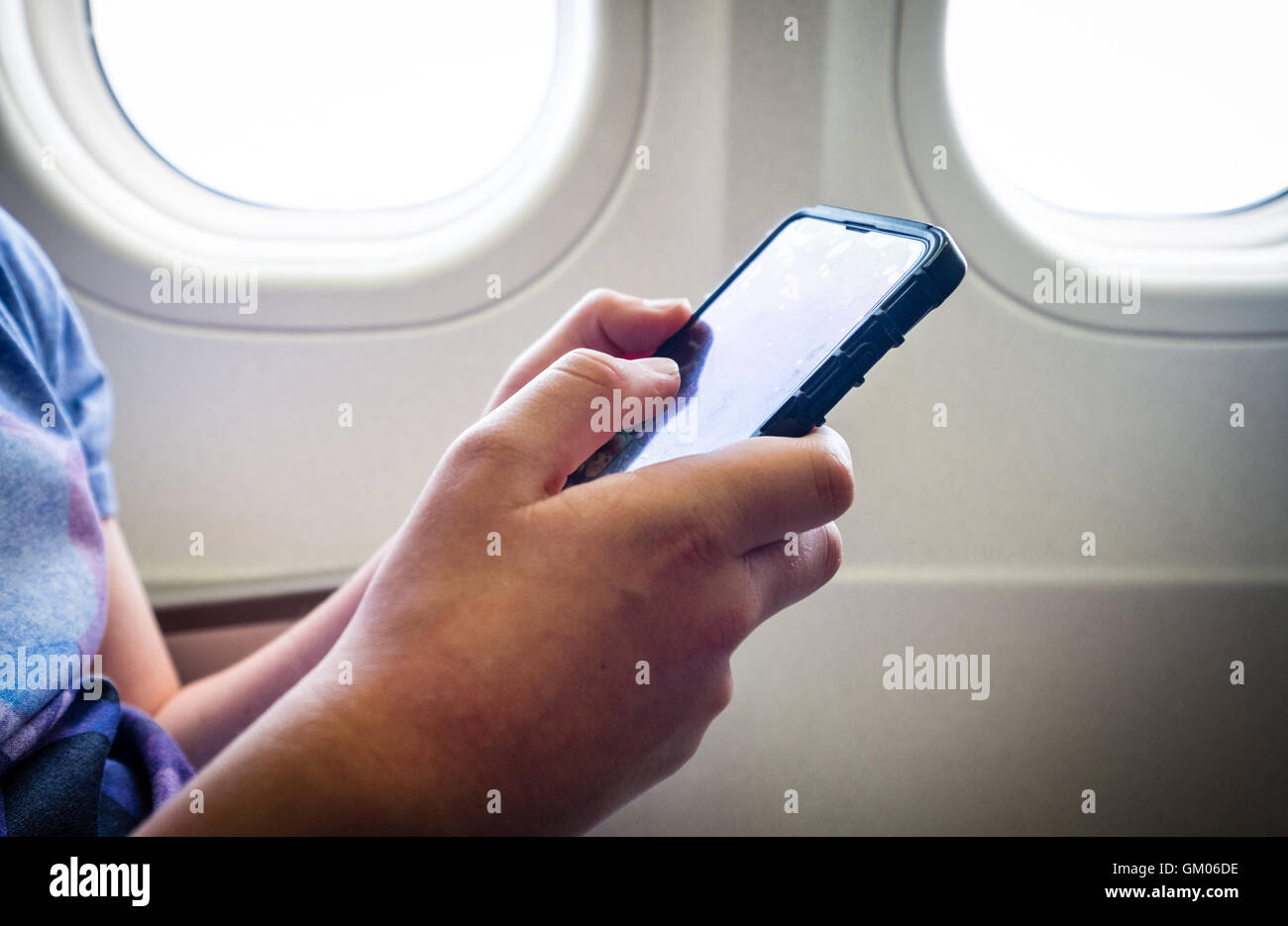 Un ragazzo adolescente utilizzando il suo telefono cellulare durante il volo su un piano Foto Stock
