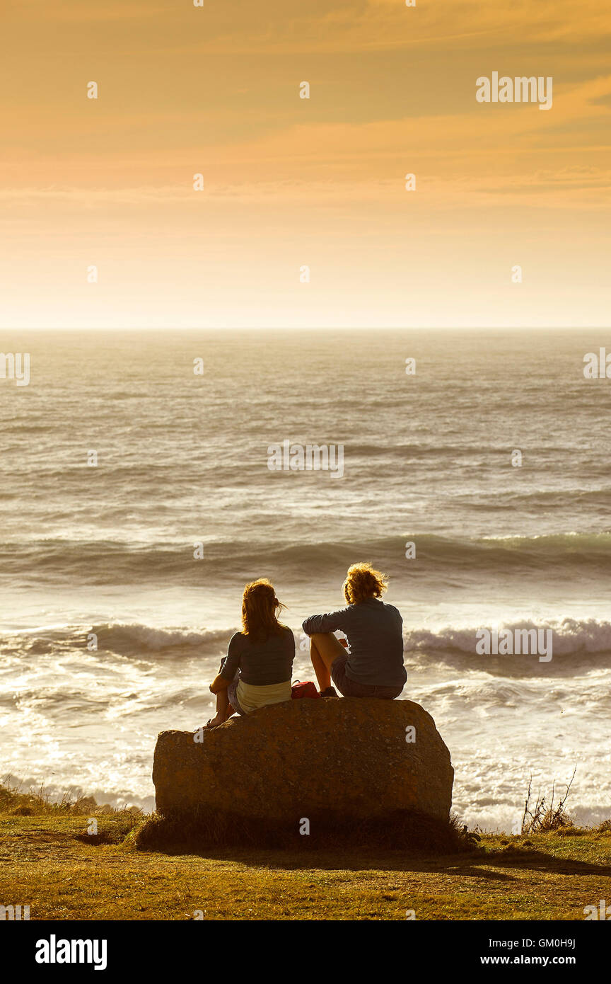 Due turisti a sedersi su una roccia e godetevi il tramonto sul promontorio in Newquay, Cornwall. Foto Stock