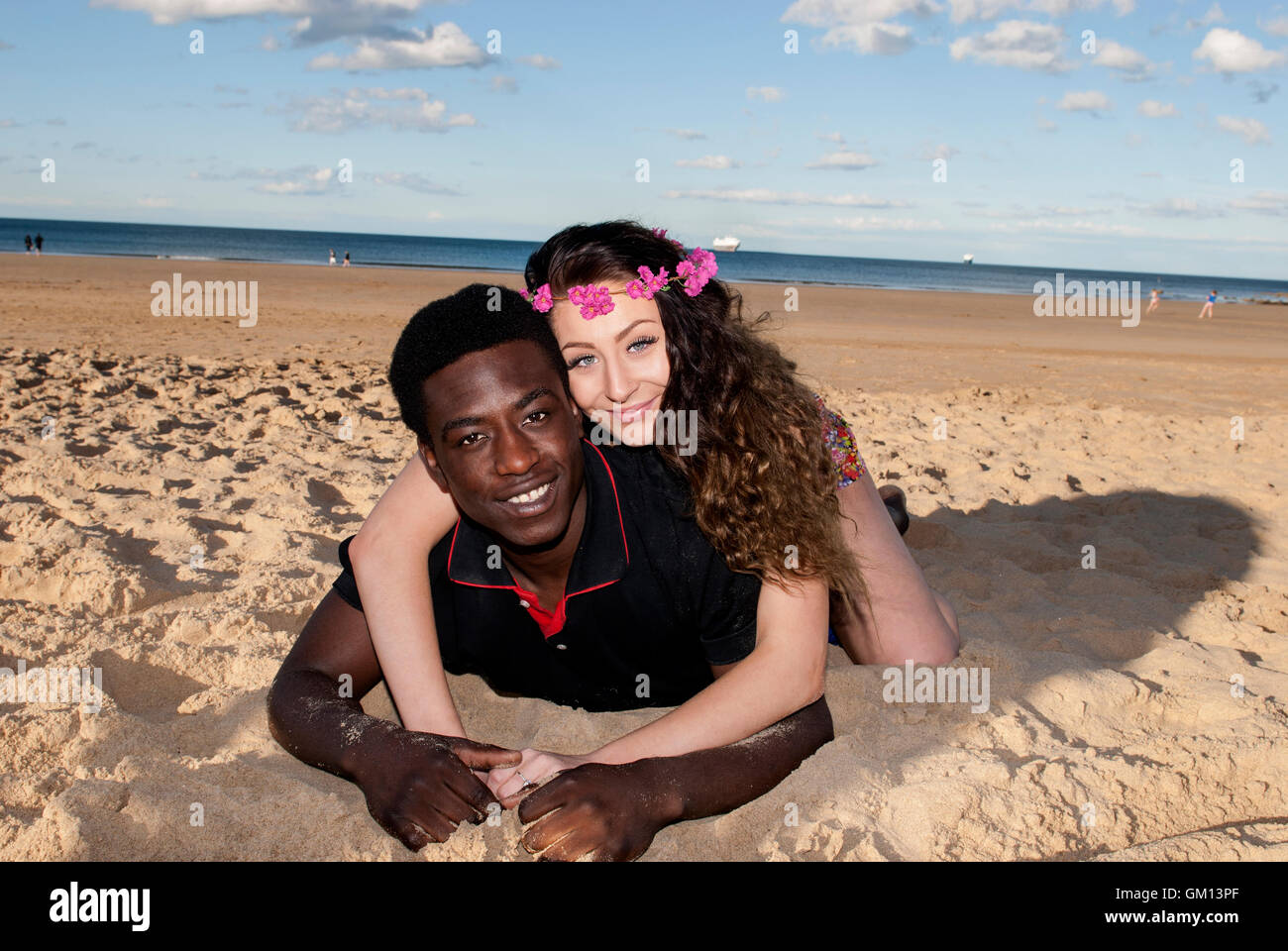 Attraente muticultural razza mista giovane giacente sulla sabbia in spiaggia costeggiata a ridere felice avendo divertimento Foto Stock