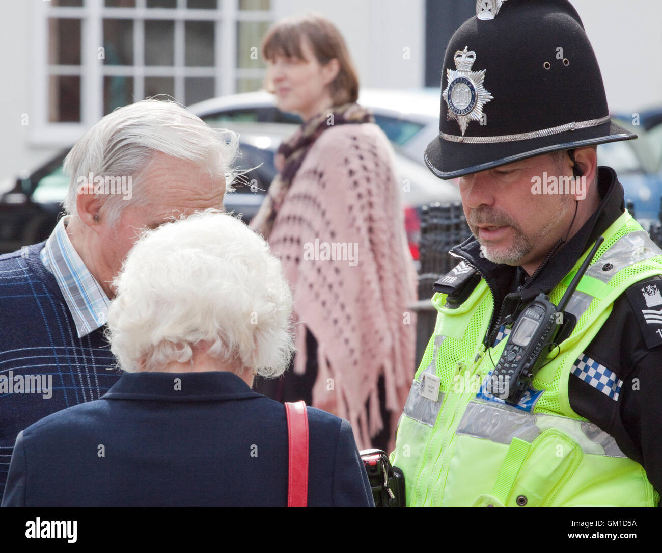 Funzionario di polizia nel casco tradizionale in conversazione con due anziani Foto Stock