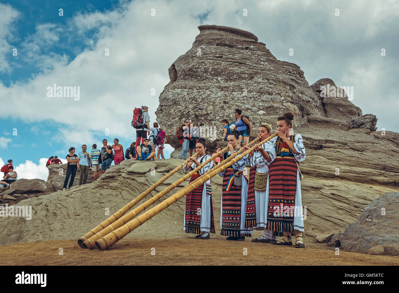 Montagne di Bucegi, Romania - 6 Agosto 2016: giovane rumeno artiste donne che indossano costumi tradizionali riprodurre il tulnic vicino alla Sfinge civiltà megalitica. Foto Stock