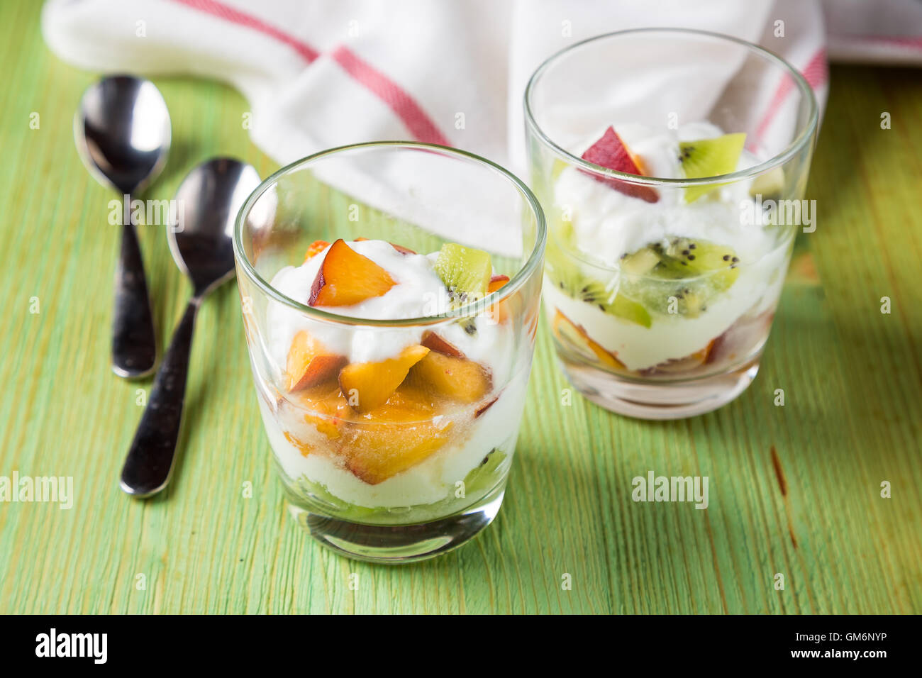 Insalata di frutta in calici in vetro di kiwi e pesche con lo yogurt sul tavolo verde Foto Stock