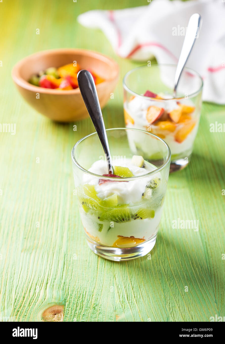 Insalata di frutta in calici in vetro di kiwi e pesche con lo yogurt sul tavolo verde Foto Stock