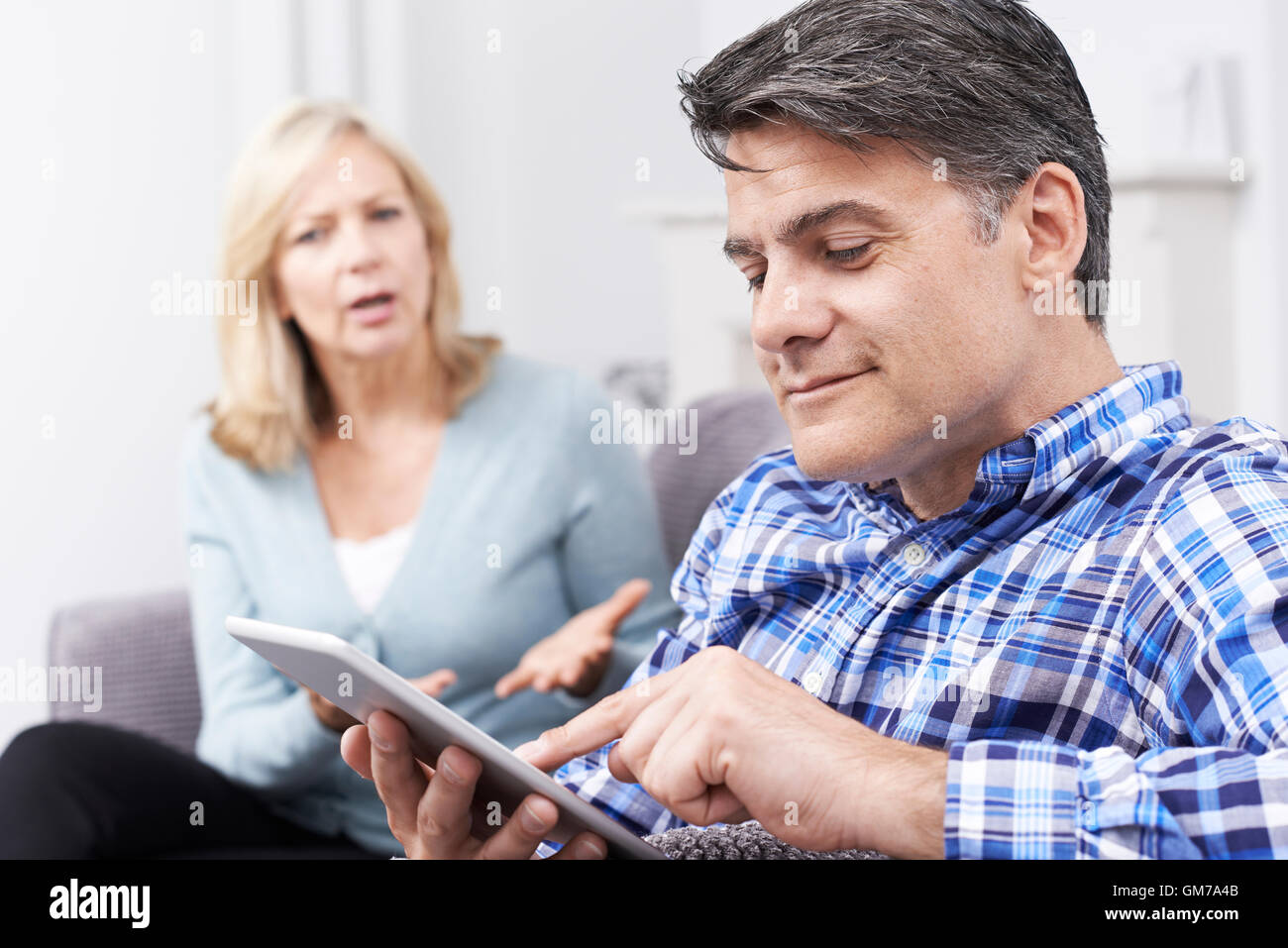 Infelice donna seduta sul divano come Partner utilizza tavoletta digitale Foto Stock