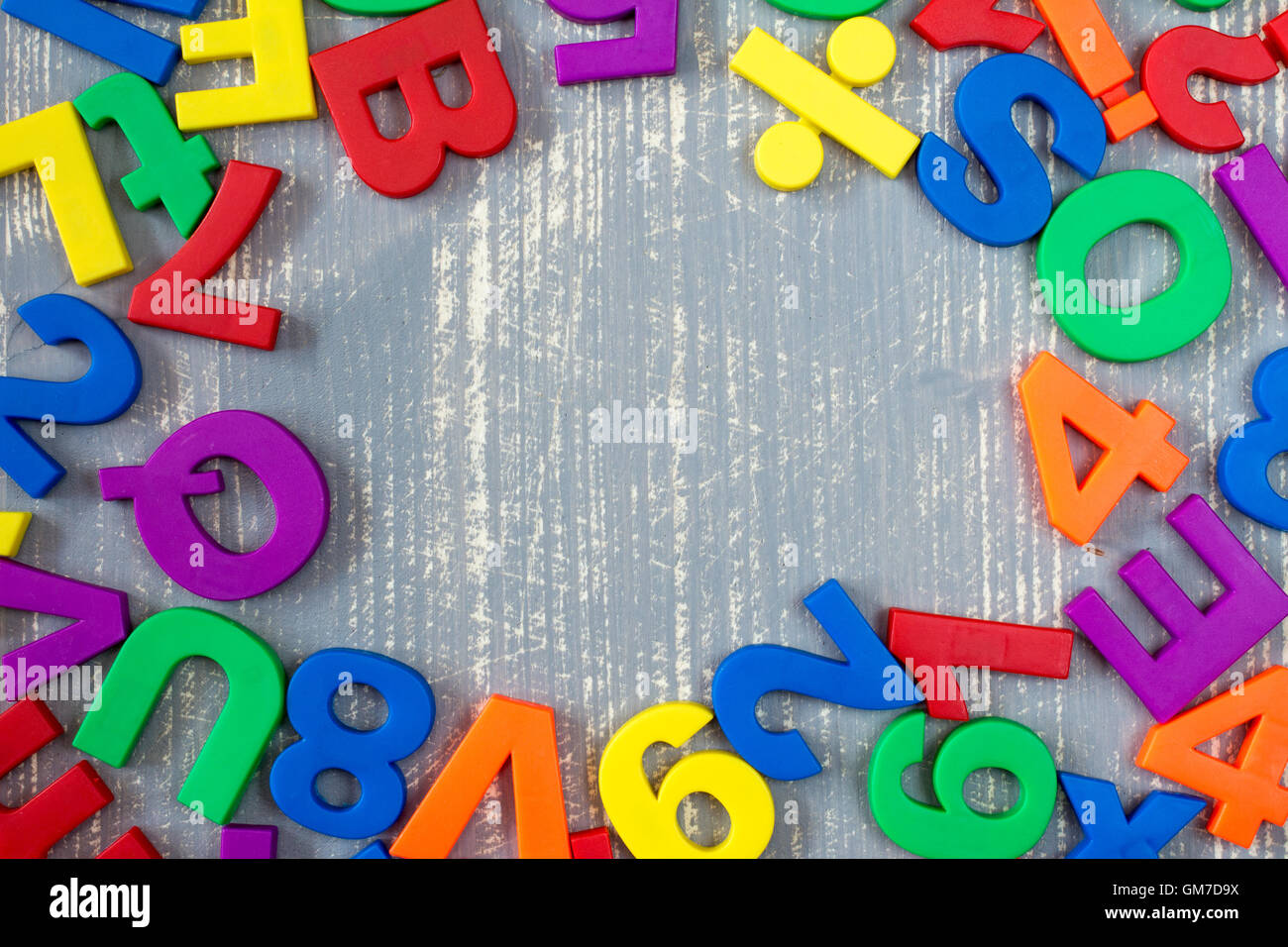 Confine di colorato magnetico giocattolo lettere e numeri nel corso di un grigio Sfondo di legno Foto Stock