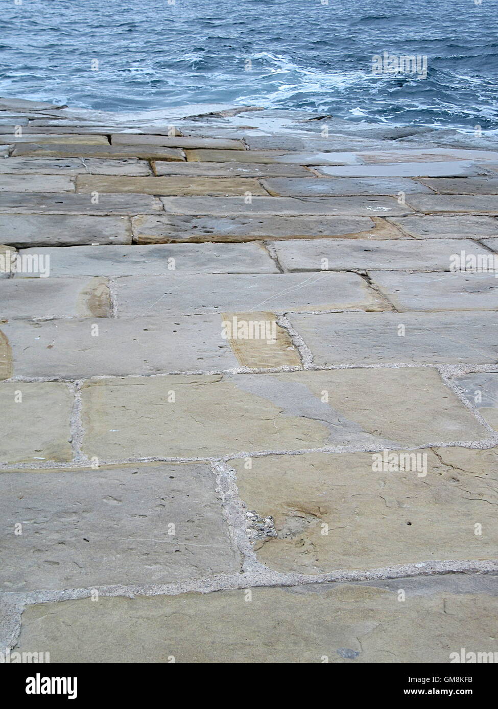 Full frame shot di marrone pavimentazione di pietra a riva e mare blu Foto Stock