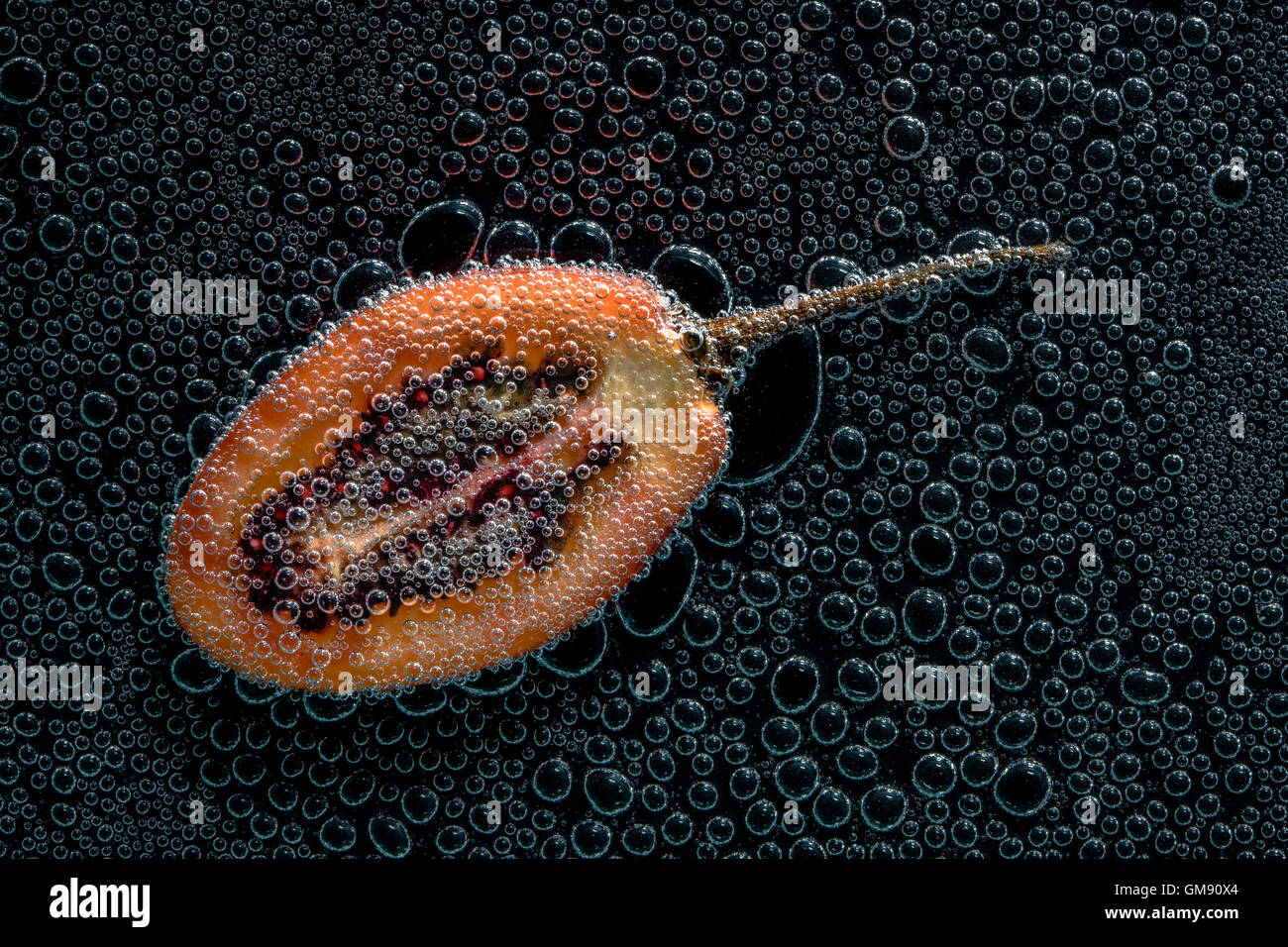 Tamarillo tagliato a metà per la frutta in acqua minerale, una serie di foto. Close-up di acqua gassata su sfondo nero Foto Stock