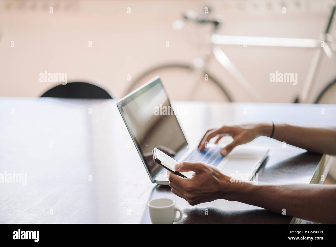 Giovane uomo che lavora sul computer portatile, guardando smart phone Foto Stock