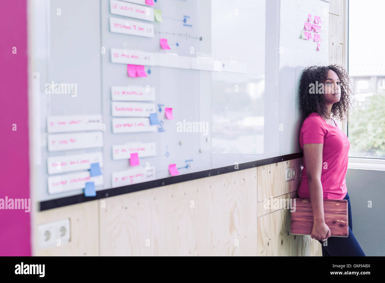 Giovane donna con il computer portatile appoggiata contro la parete in ufficio Foto Stock