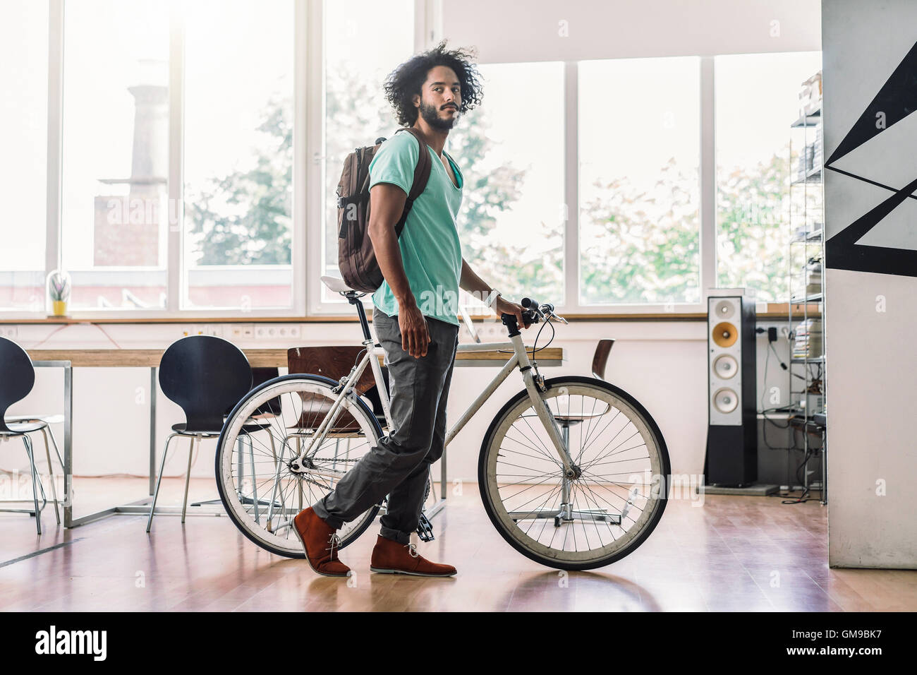Giovane uomo con zaino in spalla spingendo in bicicletta in ufficio Foto Stock