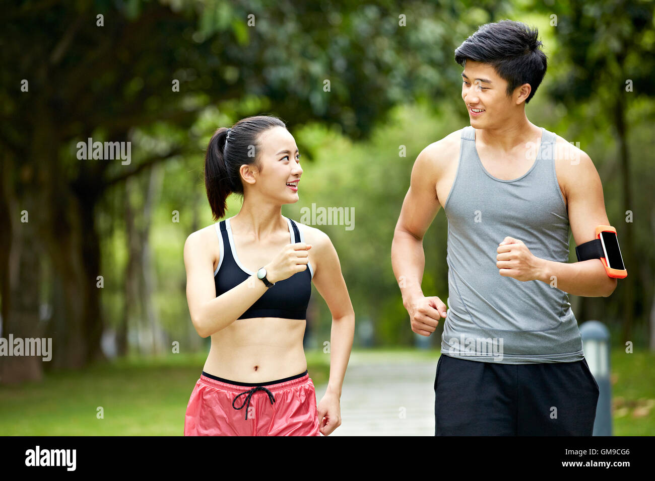 Giovane uomo asiatico e la donna giovane in esecuzione per fare jogging e parlando in un parco della città. Foto Stock