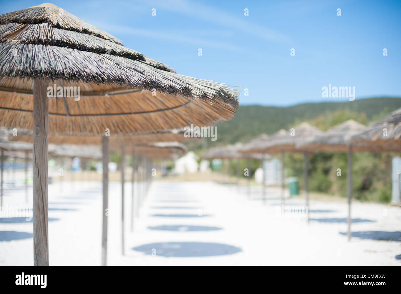 Vista offuscata di ombrellone con fuori fuoco sabbia bianca e verde paesaggio in background, nessuno sulla spiaggia nella giornata di sole Foto Stock