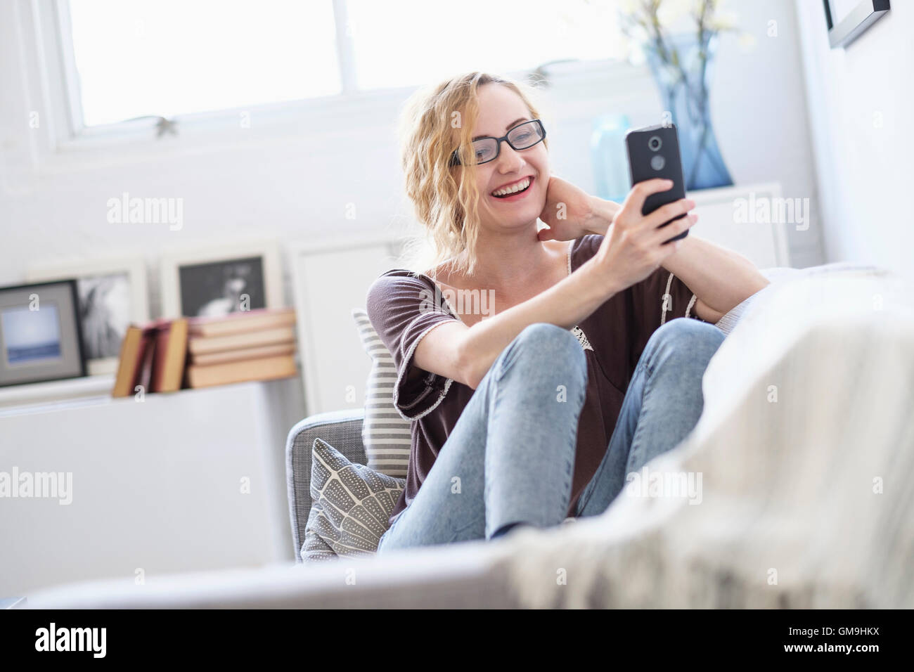 Giovane donna con aspirapolvere ricaricabile seduto sul divano e  utilizzando il cellulare a casa Foto stock - Alamy