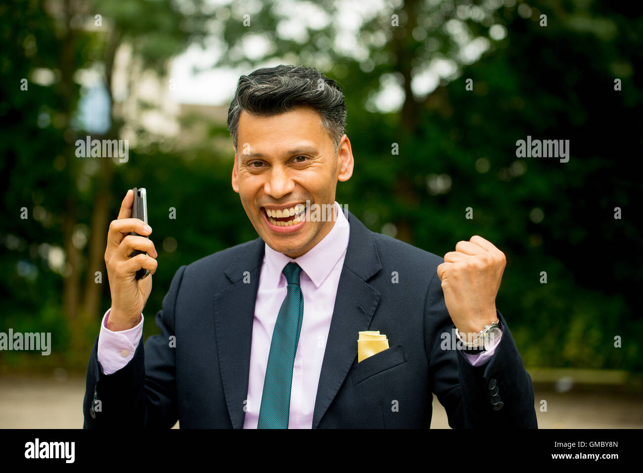 Gioioso uomo d'affari con pelle d'oliva con le braccia sollevate e tenendo il telefono cellulare in una mano. Foto Stock