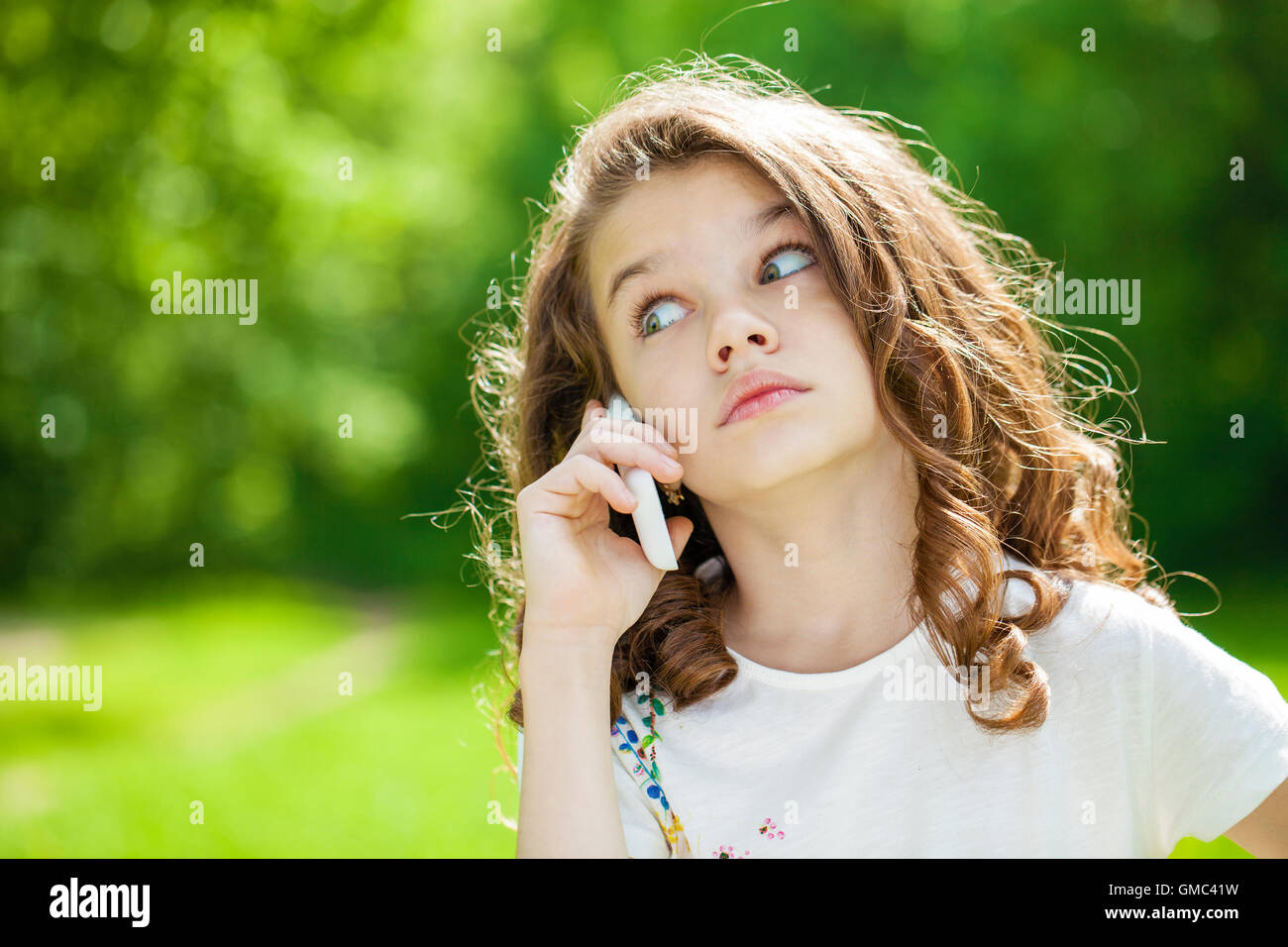 Bellissima bambina chiamando dal telefono cellulare sullo sfondo del parco di estate Foto Stock