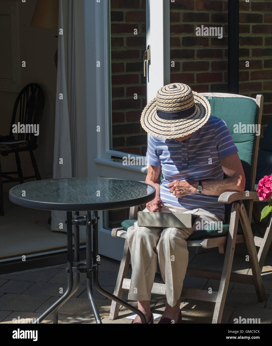 Signora matura nel cappello per il sole seduti fuori in un giardino di lettura, REGNO UNITO Foto Stock