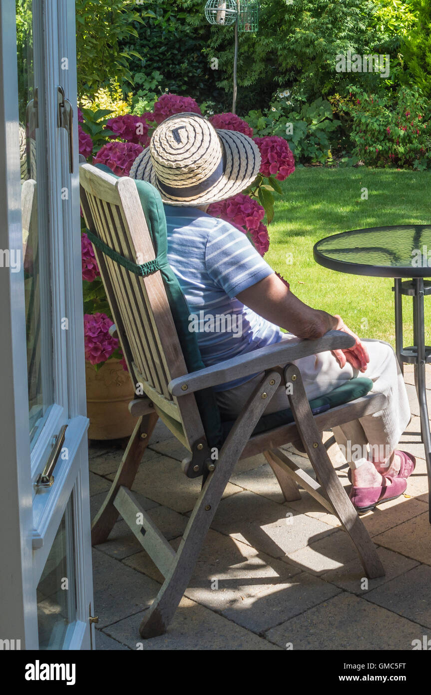 Signora matura nel cappello per il sole seduti fuori in un giardino da solo, REGNO UNITO Foto Stock