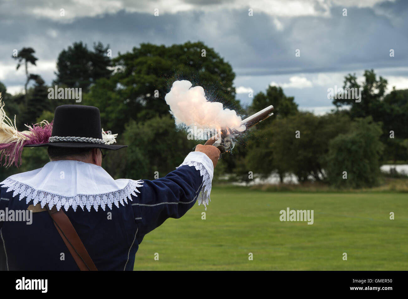 Guerra Civile Inglese Royalist soldato sparare la sua wheelock pistola militare ad una rievocazione storica, Spetchley Park, Worcestershire, Inghilterra Foto Stock