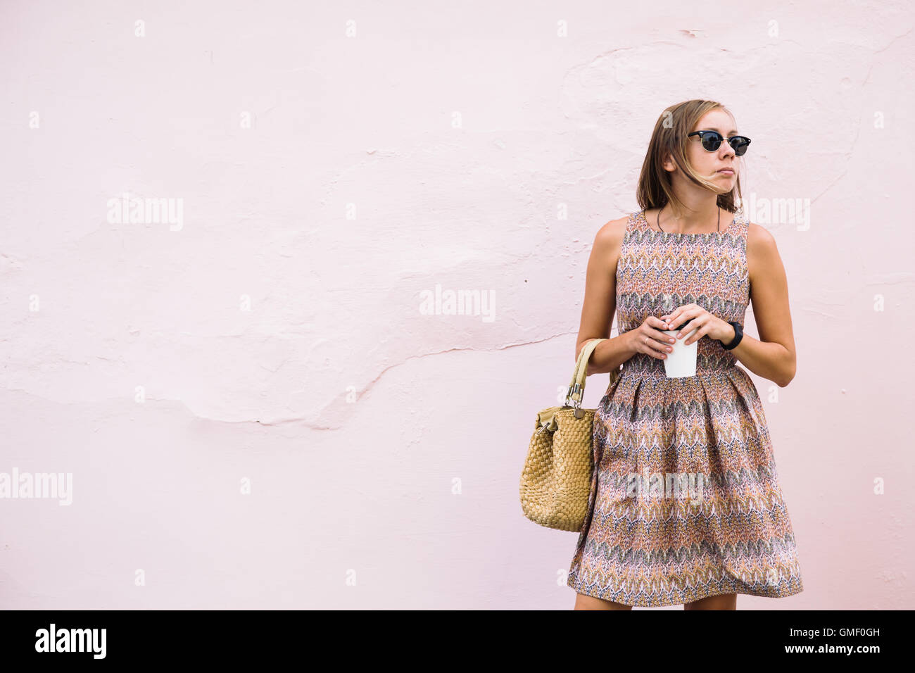Elegante giovane donna con il caffè per andare sulla luce parete rosa Foto Stock