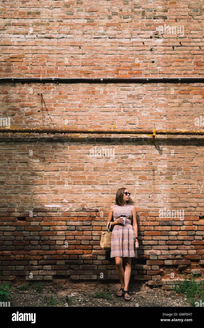 Giovane donna in abito con caffè di andare contro di brickwall Foto Stock
