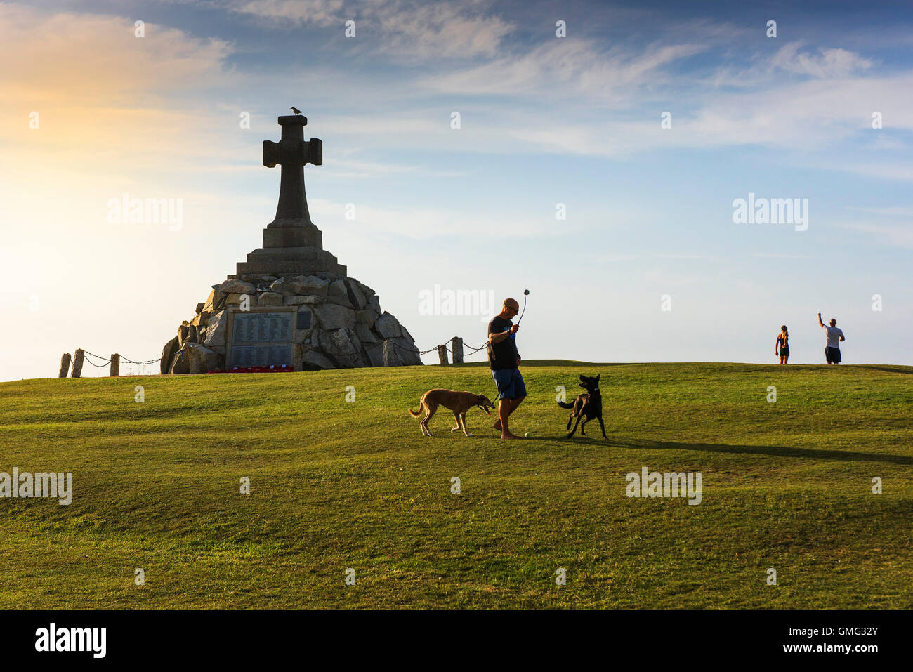Un uomo gioca con i suoi due cani di fronte al Newquay War Memorial, Cornwall. Foto Stock