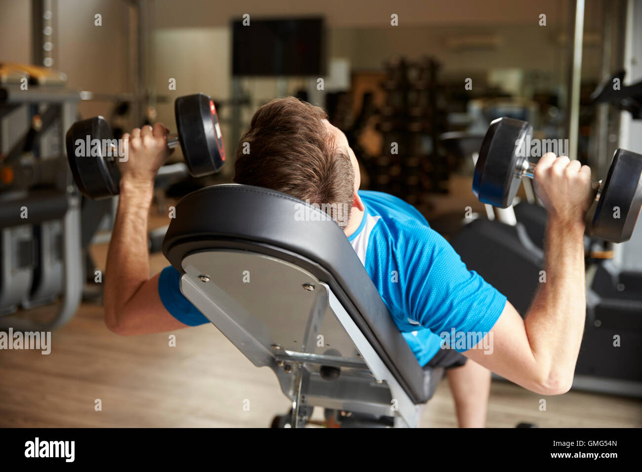 L'uomo lavora con pesi su un banco in una palestra, vista posteriore Foto Stock