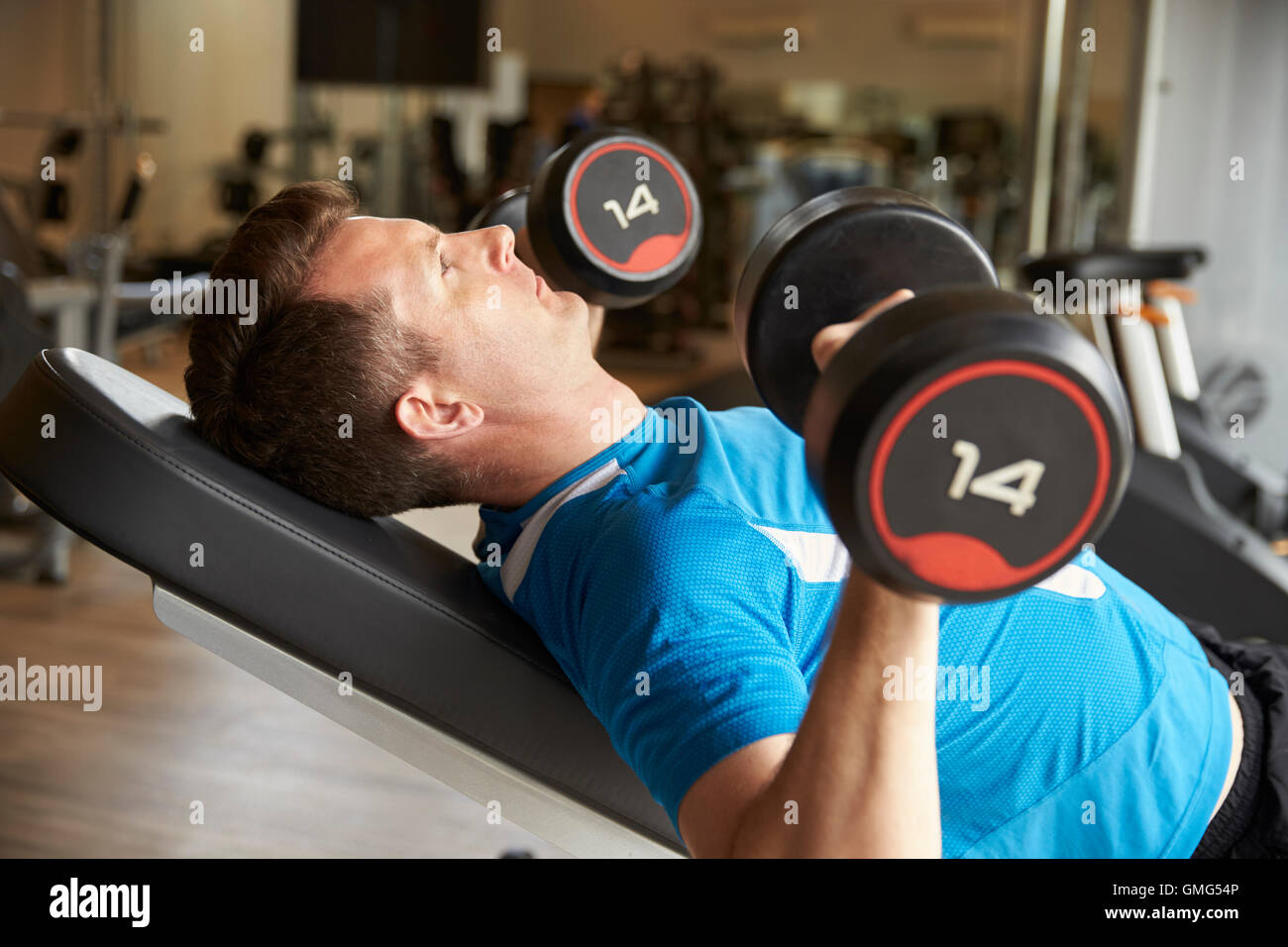 L'uomo lavora con pesi su un banco in una palestra, vista laterale Foto Stock