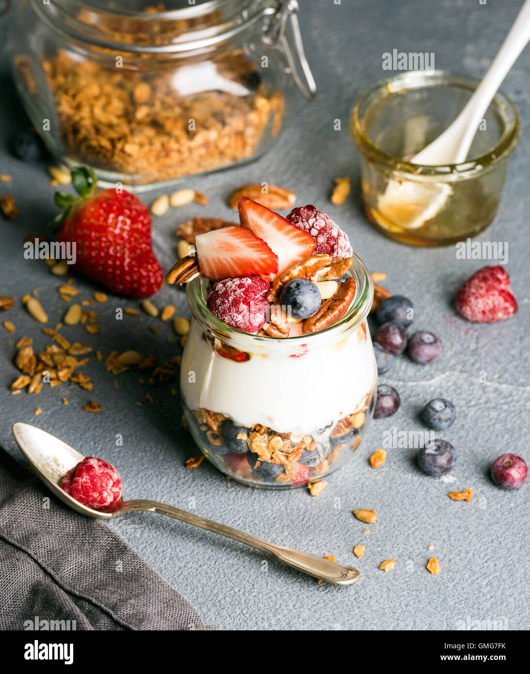 Yogurt oat granola con frutti di bosco freschi, noci, miele e foglie di menta in un barattolo di vetro sul cemento grigio Sfondo testurizzata Foto Stock