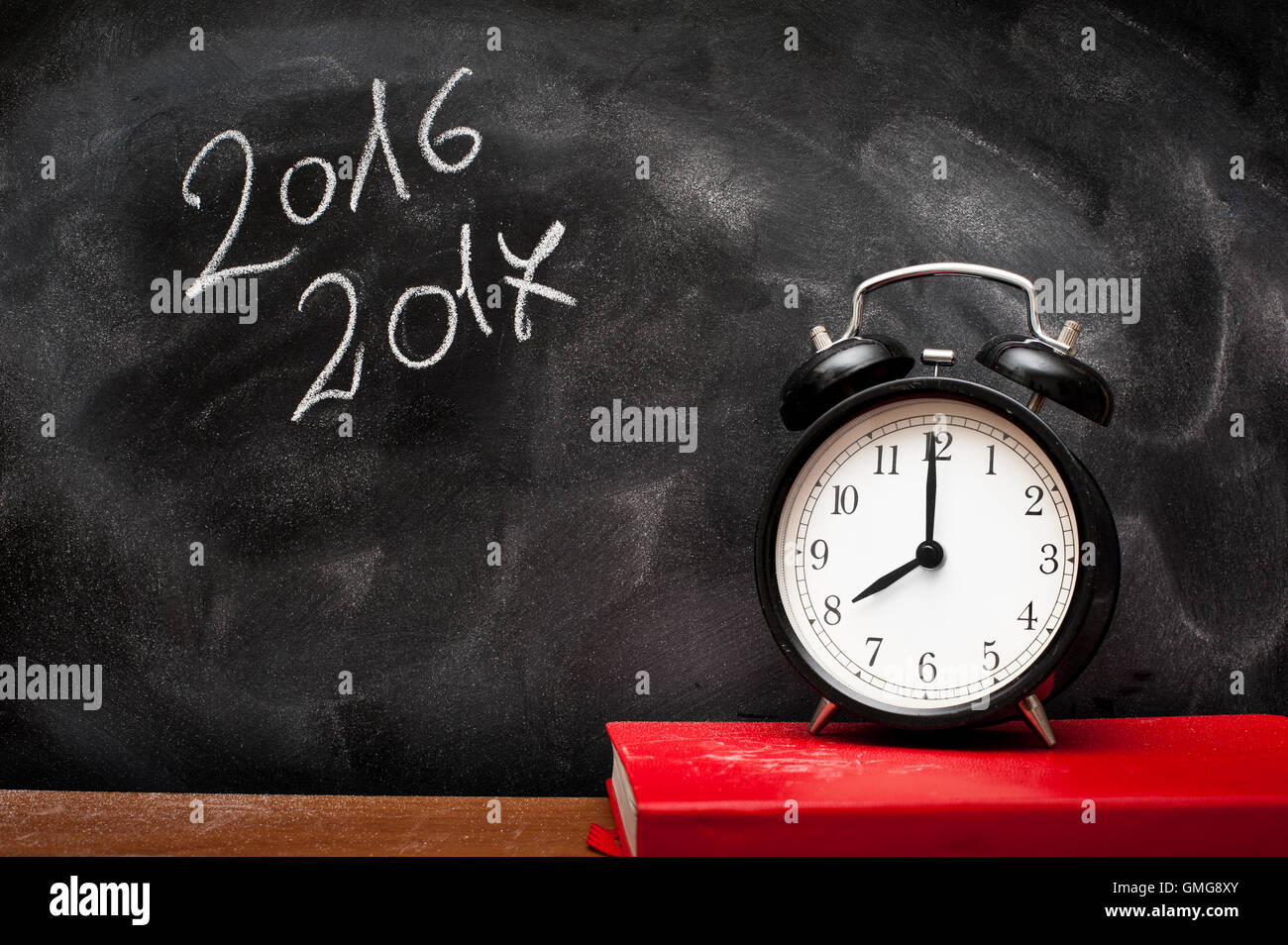 Numero 2016 e 2017 scritto su polverosi scheda scuola con sveglia e notebook rosso Foto Stock