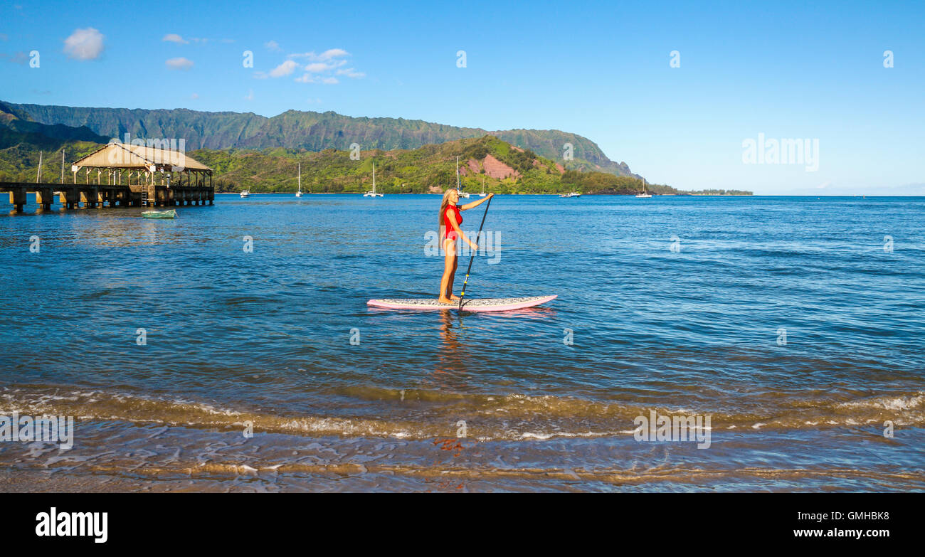 Donna stand up paddling in Hanalei Bay nei pressi del molo di Hanalei Foto Stock