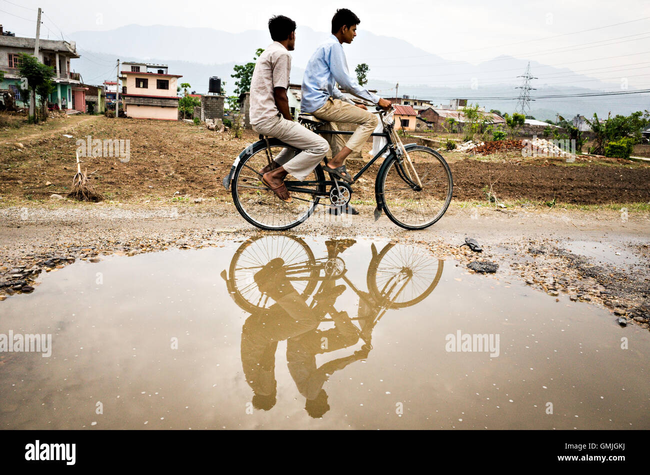 Due terai Nepalese uomo su una bicicletta che riflette su un fossato acqua, Hetauda, Nepal Foto Stock