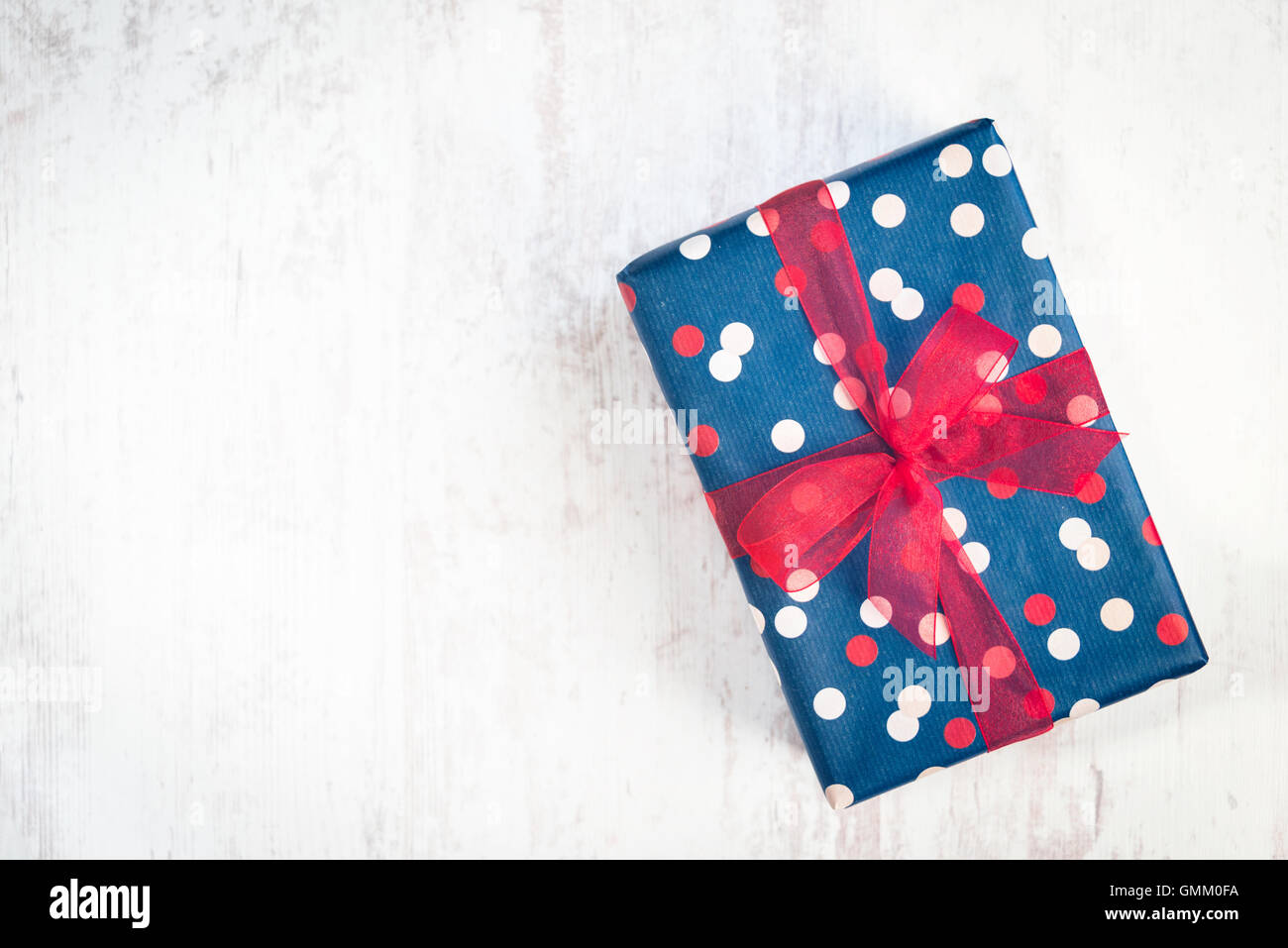 Confezione regalo avvolto in blu carta punteggiata con nastro rosso su di un legno bianco sfondo vecchio Foto Stock