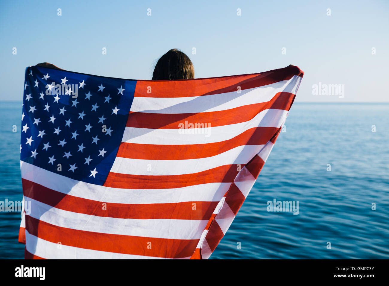 Vista posteriore della femmina con bandiera americana contro il mare Foto Stock
