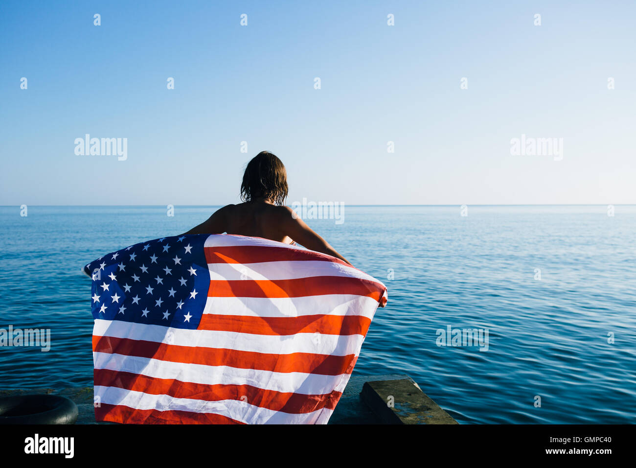 Vista posteriore della femmina con bandiera americana contro il mare Foto Stock