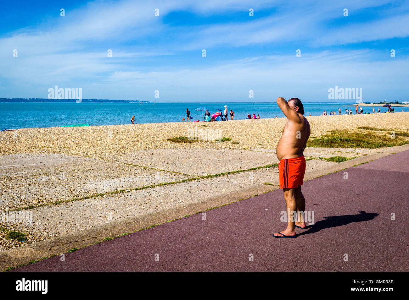 Un uomo si affaccia al mare vestito in un costume da bagno che si trova sotto il suo stomaco. Foto Stock