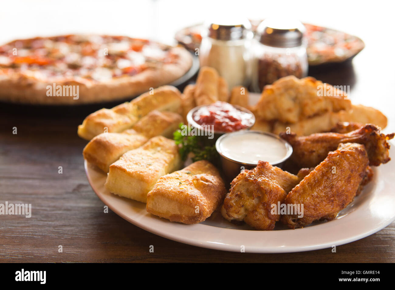 Piatto di antipasti tra cui ali di pollo, grissini e ranch dressing, con pizza in background Foto Stock