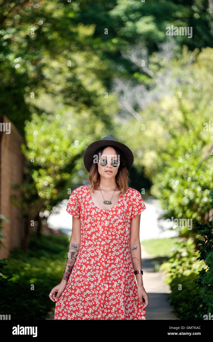 Ragazza in rosso vestito floreale con occhiali da sole e cappello, gioielli e tatuaggi al di fuori Foto Stock